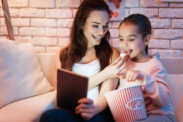 Madre e hija viendo películas en tabletas comiendo palomitas de maíz por la noche en casa . —  Fotos de Stock