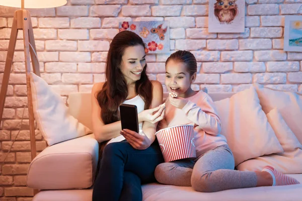 母亲和小女儿看电影在电话吃爆米花在晚上在家 — 图库照片