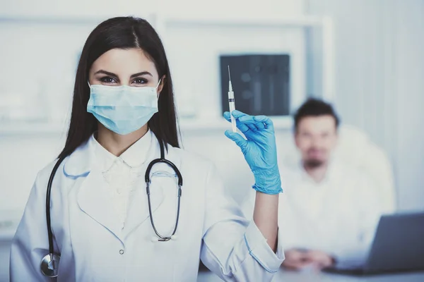 Bir şırınga ile Yardımcısı doktor. Doktor oturur masada arka planı — Stok fotoğraf