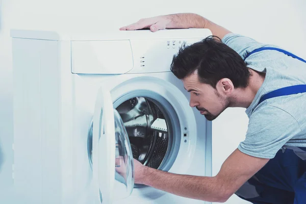Ремонтник чинит стиральную машину на белом фоне — стоковое фото