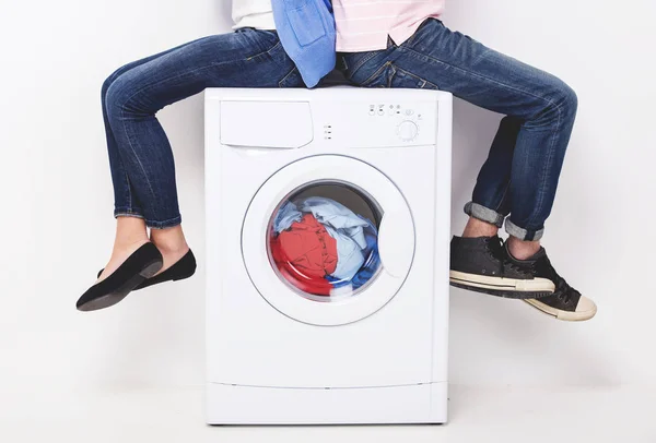 Casal jovem está sentado na máquina de lavar roupa, no fundo branco — Fotografia de Stock