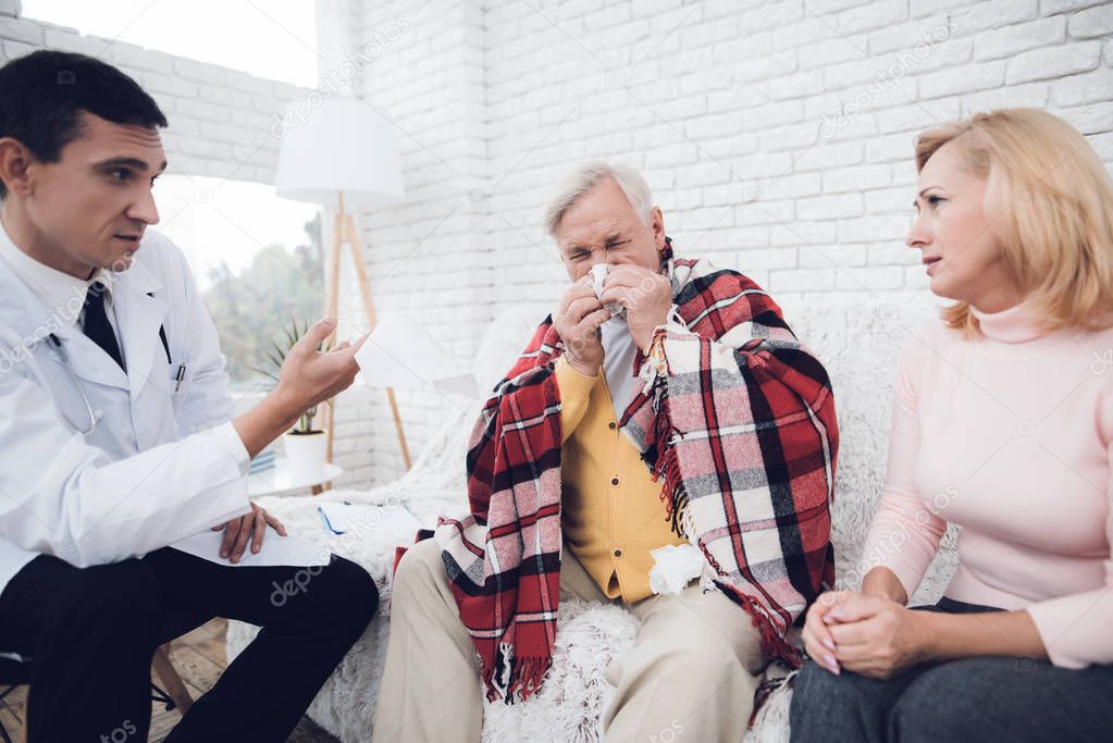 A doctor came to the old man in a yellow cardigan. The doctor communicates with the old man's wife, who sits next to him and blows his nose. They are in the house of an elderly couple.