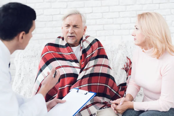 A doctor came to the old man in a yellow cardigan. The old man became ill and the doctor interrogates him. Next to him is the old man's wife. They are in the house of an elderly couple.