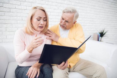 Sarı hırka bir erkekte ve kadında pembe kazak oturan ve siyah klasördeki belgeleri okuma. Onlar yüzlerinde bir şok var, onlar çok üzgün.