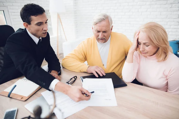 A couple of old people came to see a realtor. The old man and the woman are very upset. The realtor calm explains what is written in the documents. They are in the office of a realtor.