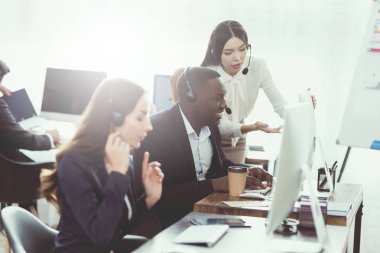 Bir kız onun meslektaşım çağrı merkezinde bir şey bilgisayar ekranında gösterir.