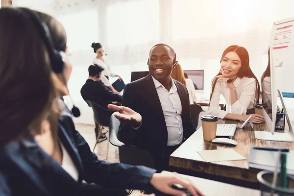 Duas garotas que trabalham como operadoras no call center conversam com um cara negro . — Fotografia de Stock