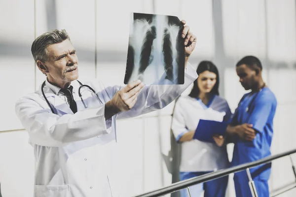 El médico mira una radiografía en el fondo son colegas — Foto de Stock