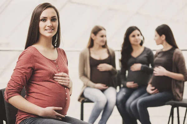 Mulher grávida bonita está olhando para a câmera. Mulheres grávidas felizes estão conversando juntas na aula de pré-natal no hospital em segundo plano — Fotografia de Stock