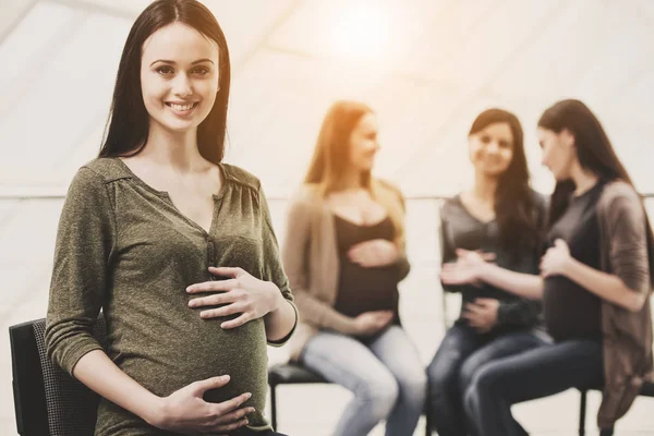 Vackra gravid kvinna tittar på kameran. Glada gravida kvinnor talar tillsammans på Prenatal klass på sjukhuset på bakgrund — Stockfoto
