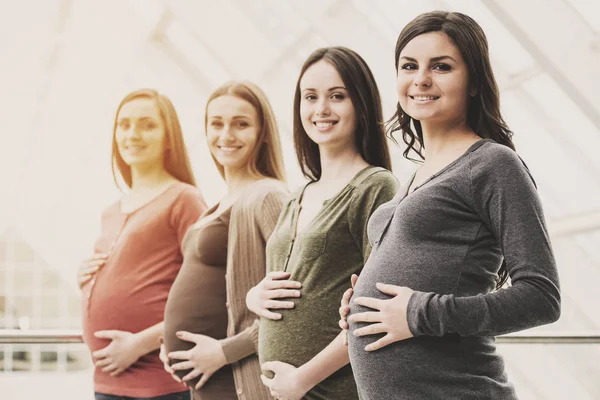 Visão lateral de quatro mulheres grávidas sorridentes estão tocando suas barrigas com as mãos. Conceito de maternidade — Fotografia de Stock