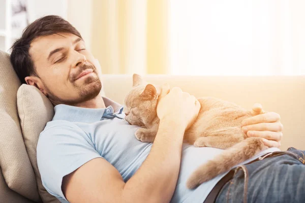 Leende ung man med hans söta katt i soffan hemma — Stockfoto