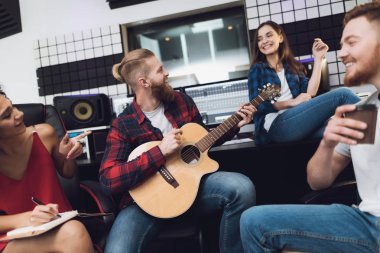 Two women and two men sing a song in a guitar in a modern recording studio. They sit behind the remote control of sound and sing a song. They are having fun.