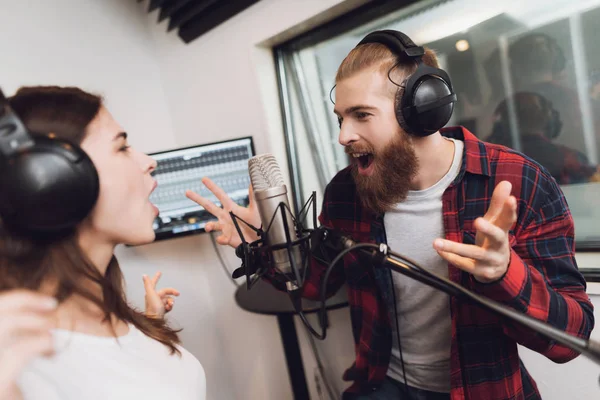 A man and a woman sing a song in a modern recording studio. On the man is a red checked shirt, on a woman a white T-shirt.