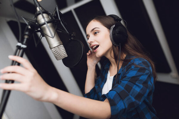 The girl sings her song in a modern recording studio. She sings the song very emotionally. In front of her is a studio microphone.