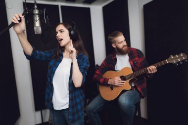 Bir kız ve bir adam bir modern kayıt stüdyosunda bir gitar için bir şarkı söyle. Kız şarkı söylüyor ve adam gitar çalıyor.