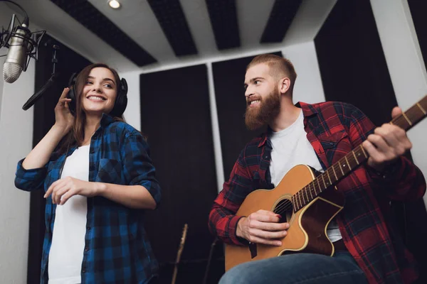 A girl and a guy sing a song to a guitar in a modern recording studio. The girl sings, and the guy plays the guitar.