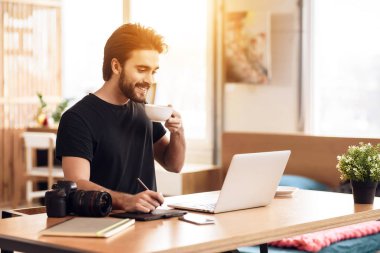 Freelancer dizüstü masa başında oturup, kahve içme adam sakallı.