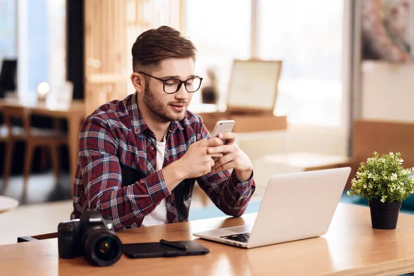 Freelancer hombre escribiendo en el teléfono en el ordenador portátil sentado en el escritorio . — Foto de Stock