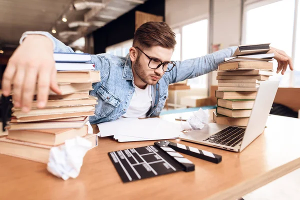 Freelancer mannen tittar på anteckningar frustrerad på laptop sitter vid skrivbord omges av böcker. — Stockfoto