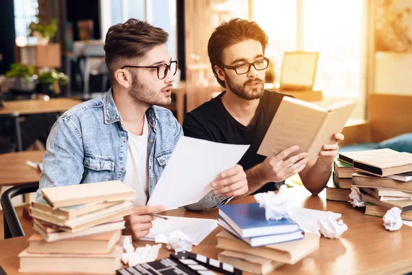 Zwei freiberufliche Männer lesen Notizen am Laptop am Schreibtisch, umgeben von Büchern. — Stockfoto