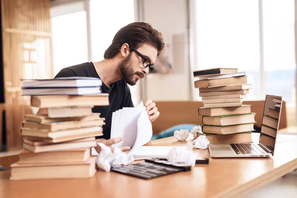 Freiberufler bärtiger Mann macht sich Notizen am Schreibtisch, umgeben von Büchern. — Stockfoto