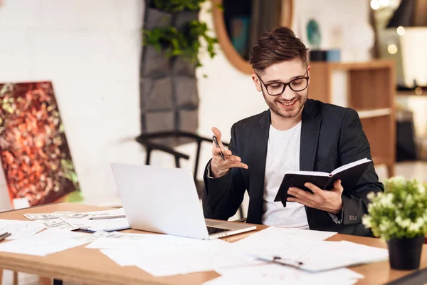 Freelancer bearded man tar anteckningar i anteckningsboken på laptop sitter vid skrivbord. — Stockfoto