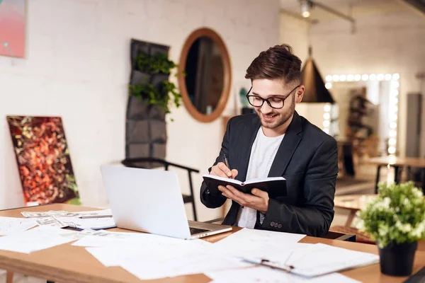 Freelancer barbudo hombre tomando notas en el portátil sentado en el escritorio . — Foto de Stock