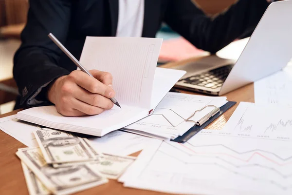 Freelancer hombre tomando notas en el cuaderno en el portátil sentado en el escritorio . —  Fotos de Stock