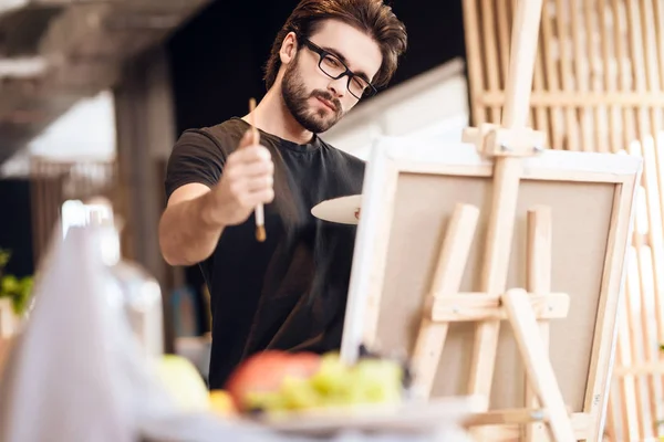 Freelancer hombre pintura con pincel de pie detrás del caballete . —  Fotos de Stock