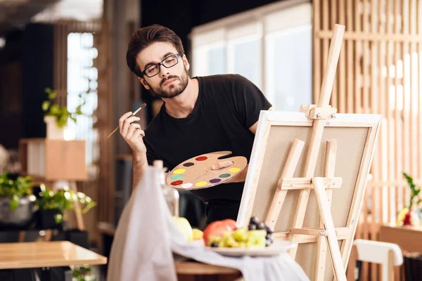 Ελεύθερος επαγγελματίας άνθρωπος ζωγραφική με πινέλο στέκεται πίσω από το καβαλέτο. — Φωτογραφία Αρχείου