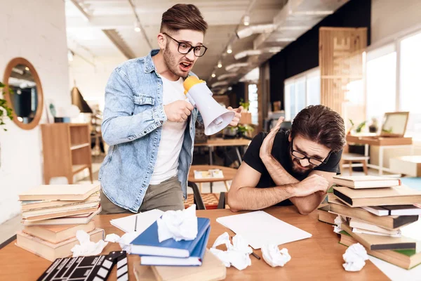 Zwei freiberufliche Männer am Schreibtisch, umgeben von Büchern, ein Mann schreit in Megafon. — Stockfoto