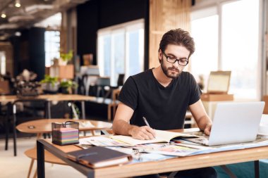 Serbest meslek sahibi adam masada oturan laptop notlar alarak sakallı.