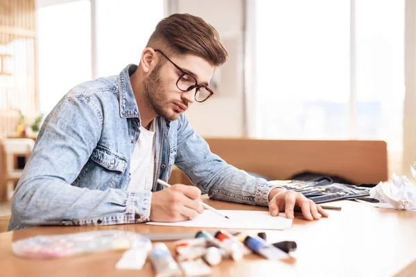 Freelancer man ritar på papper med penna som sitter vid skrivbord. — Stockfoto