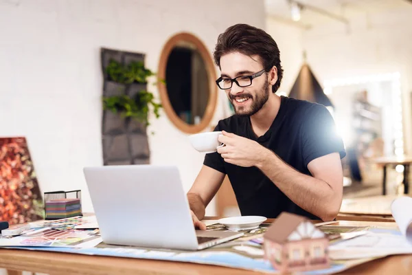 Freelancer barbudo hombre bebiendo té en el portátil sentado en el escritorio . — Foto de Stock