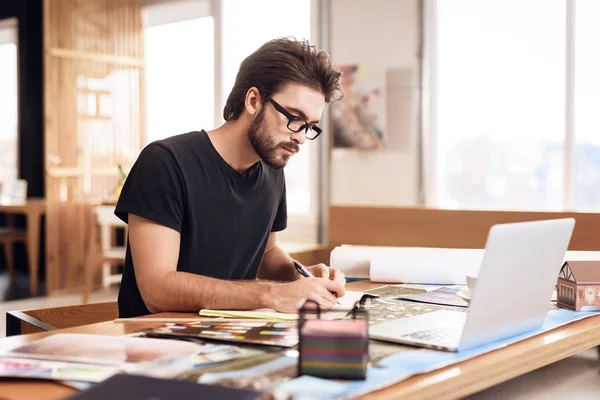 Фрилансер бородатый человек делает заметки за ноутбуком, сидя за столом . — стоковое фото