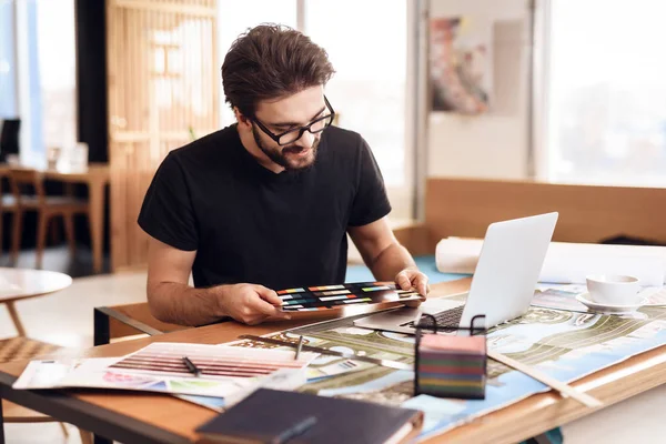 Freelancer barbudo hombre mirando muestras de color en el ordenador portátil sentado en el escritorio . — Foto de Stock