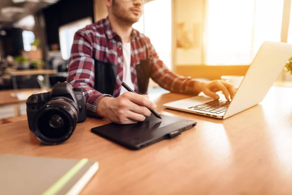 Muž na volné noze psaní a kreslení na laptop sedí u stolu. — Stock fotografie