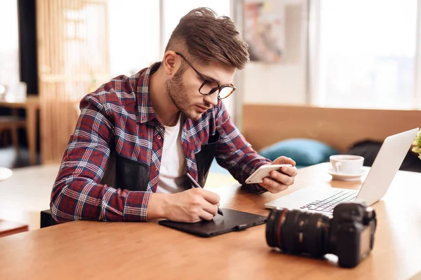 Freelancer hombre dibujo en la tableta en el ordenador portátil sentado en el escritorio . — Foto de Stock