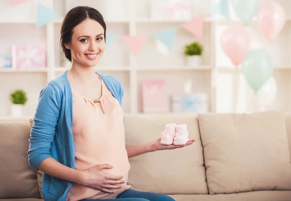 Красивая беременная женщина держит маленькие ботинки для будущего ребенка — стоковое фото