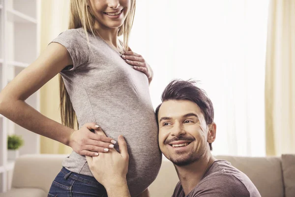 Husband is listening to his pregnant wife's belly at home — Stock Photo, Image