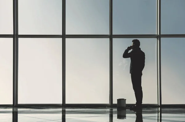 Silueta vista del joven empresario está de pie en la oficina moderna con ventanas panorámicas — Foto de Stock