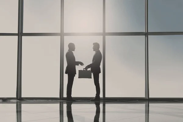 Sylwetka widok dwóch młodych przedsiębiorców stojących z walizka w nowoczesne biuro z panoramicznymi oknami — Zdjęcie stockowe