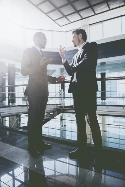 Two young businessmen are talking while standing at modern office — Stock Photo, Image