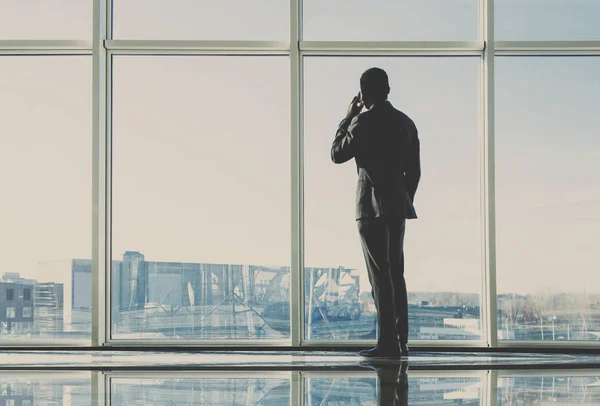 Back view of young businessman is looking out of a panoramic window and talking by phone — Stock Photo, Image