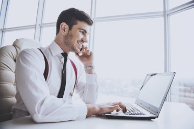 Gülümseyen iş adamı onun laptopunda ofisinde çalışıyor ve telefon konuşma