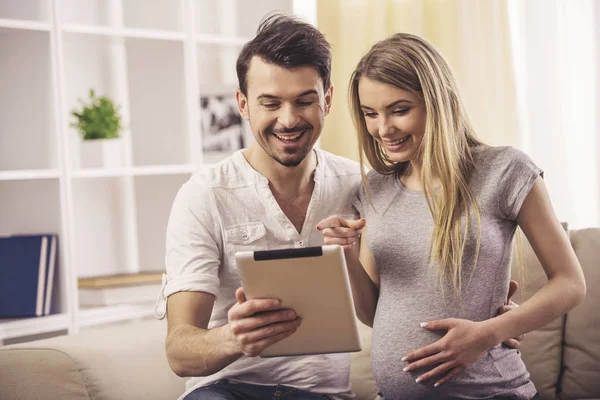 Porträt eines Mannes sitzt auf dem Sofa, während er mit seiner schwangeren Frau ein digitales Tablet benutzt — Stockfoto