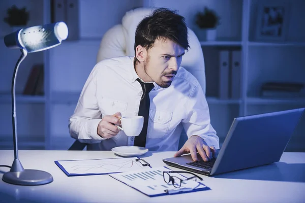 Surprised man is working on laptop in office and drinking a coffee. — Stock Photo, Image