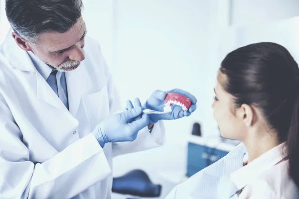 Alegre dentista enseñando en el modelo de dientes humanos cómo derecho a cepillar los dientes de su paciente femenino —  Fotos de Stock
