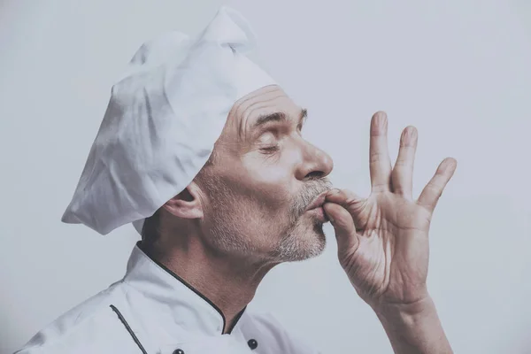 Starší muž šéfkuchař v uniformě na šedém pozadí — Stock fotografie